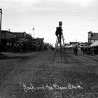 Alberta Pyatt took this photograph of Fourth Avenue, Anchorage,  around 1916 or 1917.  Visible on the right, just beyond the awnings, is the sign for the Union Cafe, where Balios worked as a cook.  Artist and photographer Sydney Laurence stands on a ladder in the center of the street to use a huge tripod supporting a large camera.