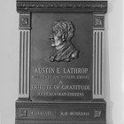 Bust of Austin E. "Cap" Lathrop.  From front, the inscription reads:  "Austin E. Lathrop, builder of a northern empire.  A tribute to gratitude from Alaskan citizens.  Fairbanks A.D. MCMXXXIX."  1939.  The bust was modeled by Piertro Vigno, a Fairbanks artist, from a photograph.  The plaque was placed in the studio of radio station KFAR, Fairbanks, and unveiled during dedication ceremonies held on October 2, 1939.
