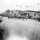 A marching band passes by Isidore "Ike" Bayles' clothing store on Fourth Avenue, ca. 1940-1950.