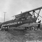 A Travel Air 7000, one of the first two planes owned by Anchorage Air Transport, a company owned by a number of Anchorage businessmen in the late 1920s.  The plane often landed or took off from the Anchorage Park Strip, which was used as a landing field before Merrill Field was built.  The figure working the propeller has been identified as pilot Russel Merrill.