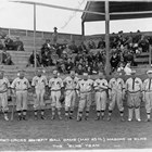 Christian "Chris" Eckmann, the fifth man from the right, playing for the Elks against the Masons on May 25, 1918.  Eckmann holds a baseball bat in his right hand, running down his right leg.  Baseball was very popular in early Anchorage; the ballpark was where the Anchorage Museum now stands.