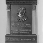 Bust of Austin E. "Cap" Lathrop. From front, the inscription reads: "Austin E. Lathrop, builder of a northern empire. A tribute to gratitude from Alaskan citizens. Fairbanks A.D. MCMXXXIX." 1939. The bust was modeled by Piertro Vigno, a Fairbanks artist, from a photograph. The plaque was placed in the studio of radio station KFAR, Fairbanks, and unveiled during dedication ceremonies held on October 2, 1939.