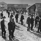 Arthur A. Shonbeck is identified as the tall man with his hands in his pockets, standing on the left of the group of men in right front.  The photograph was taken of Anchorage residents strolling around the buildings that Austin E. "Cap" Lathrop built at the end of Third Avenue in Anchorage as a movie studio where part of "The Chechakos" was filmed in 1924.  