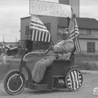 William A. C. “Lucky” Baldwin became incapacitated later in life, and was known for riding around Anchorage in his motorized wheelchair.  Here he has the wheelchair decorated for a parade during the mid to late 1930s, touting President Franklin Roosevelt’s New Deal program.