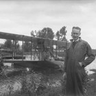 Russel Hyde Merrill standing in front of the Curtiss Model F. Seagull seaplane in which he and fellow pilot Roy J. Davis flew to Alaska and Anchorage.  The plane was severely damaged by waves caused by a storm in Cook Inlet; the remains of the airplane remained in Anchorage for at least another five years.